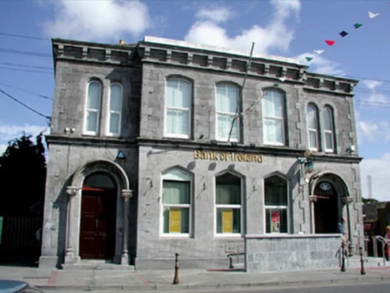 A two-storey cut limestone building on a corner, round-headed windows, the words Bank of Ireland cut into the frieze.